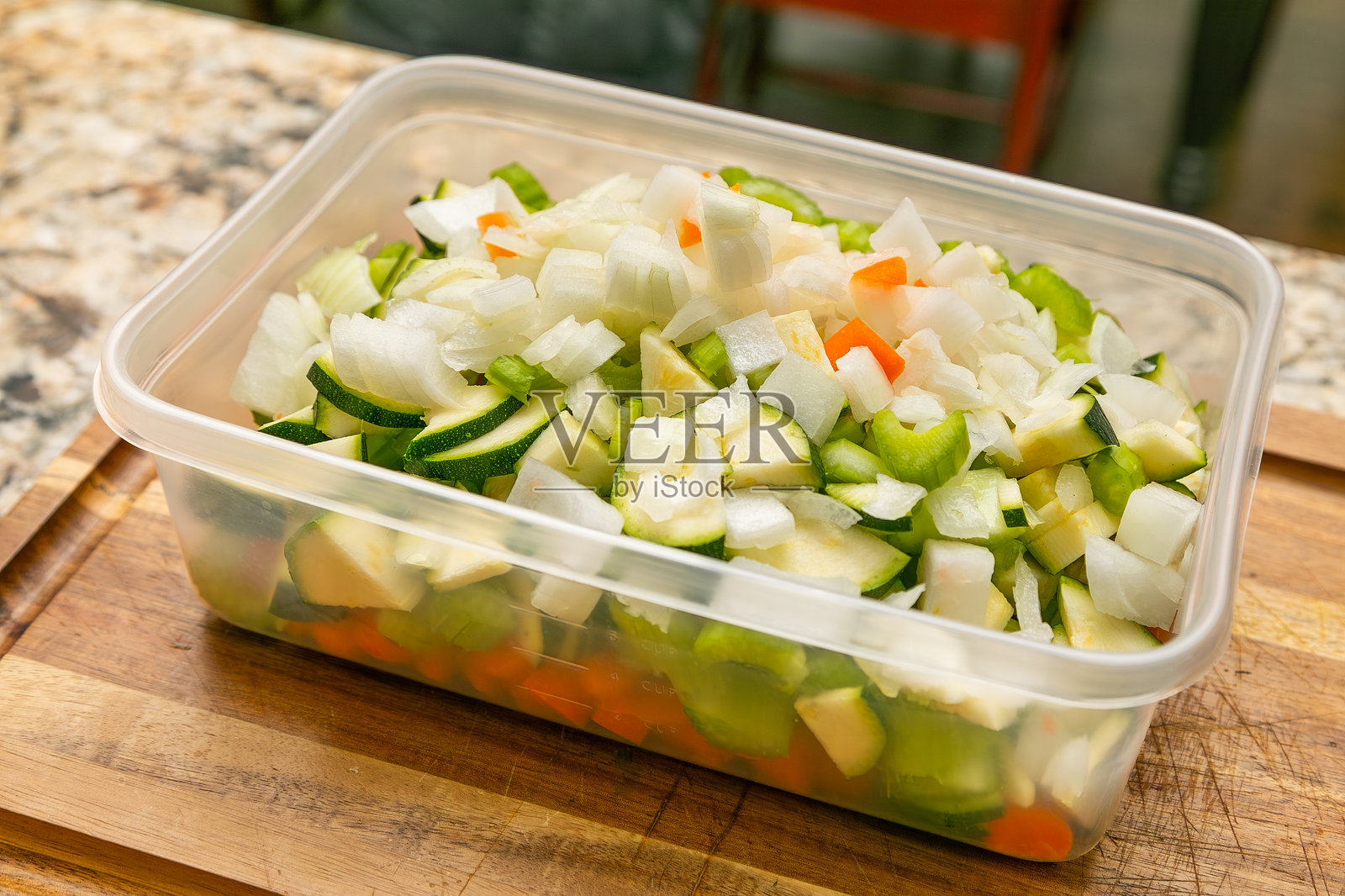 厨房木砧板上放着一个长方形塑料容器,里面装满切好的蔬菜的特写。照片摄影图片