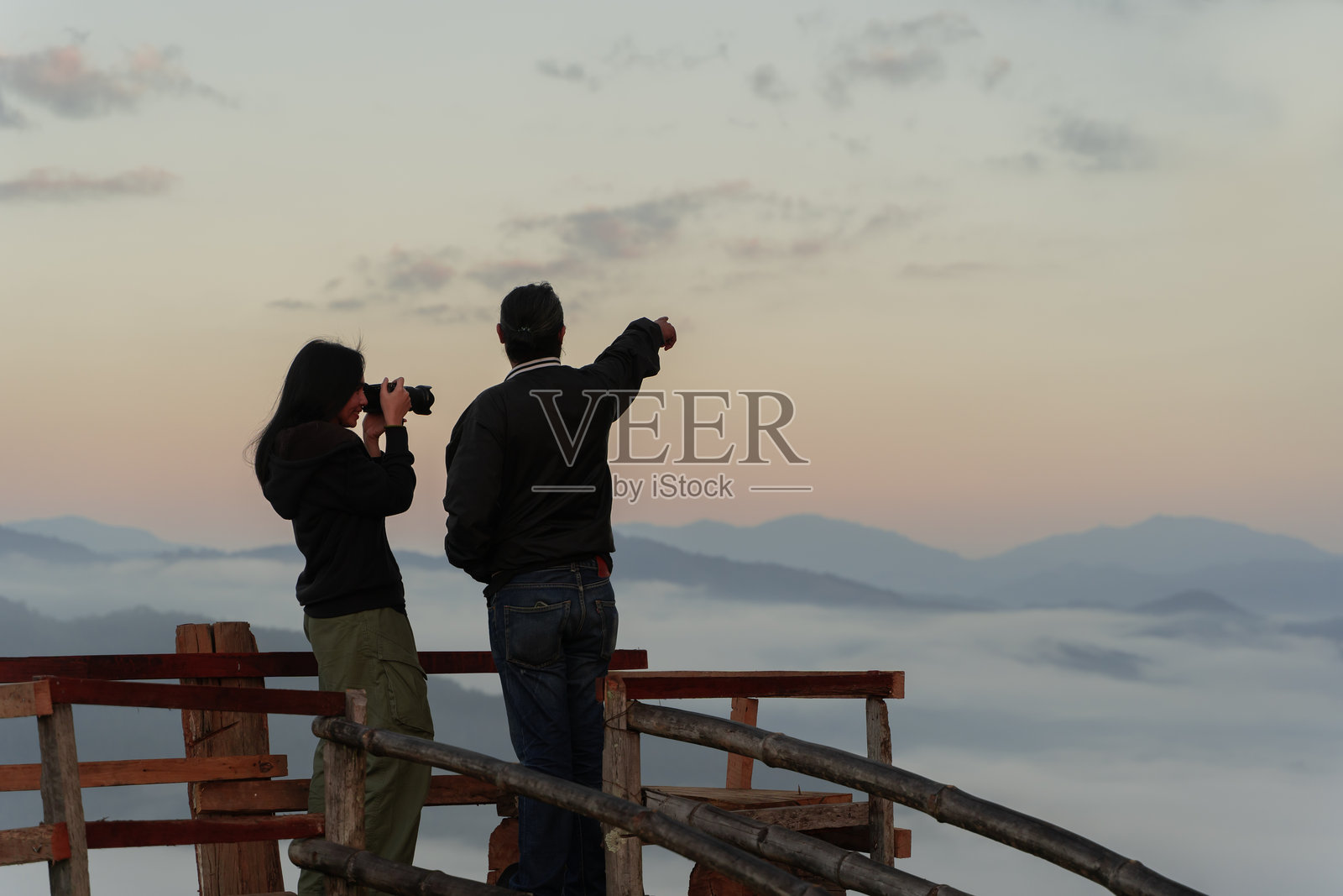 快乐的年轻情侣在高山的观景点上,手持相机欣赏雾海景观照片摄影图片