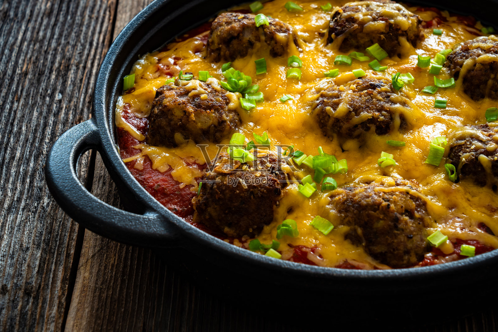 牛仔肉丸与切达奶酪一起在木桌上的煎锅中烘烤照片摄影图片