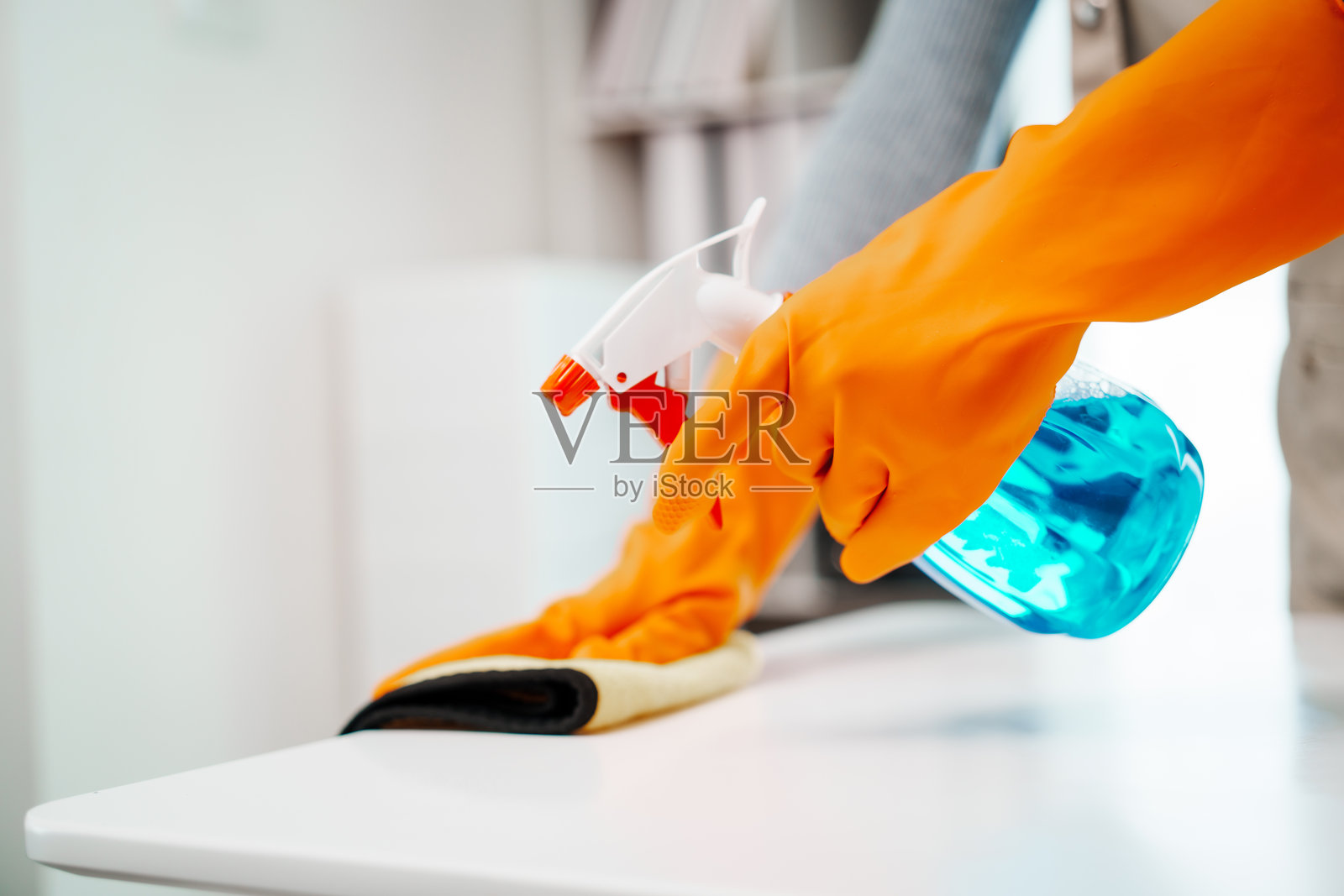 一位年轻女性穿着围裙,手持喷雾瓶和超细纤维布,准备清洁电脑屏幕并检查她的工作桌,确保工作空间整洁有序。照片摄影图片