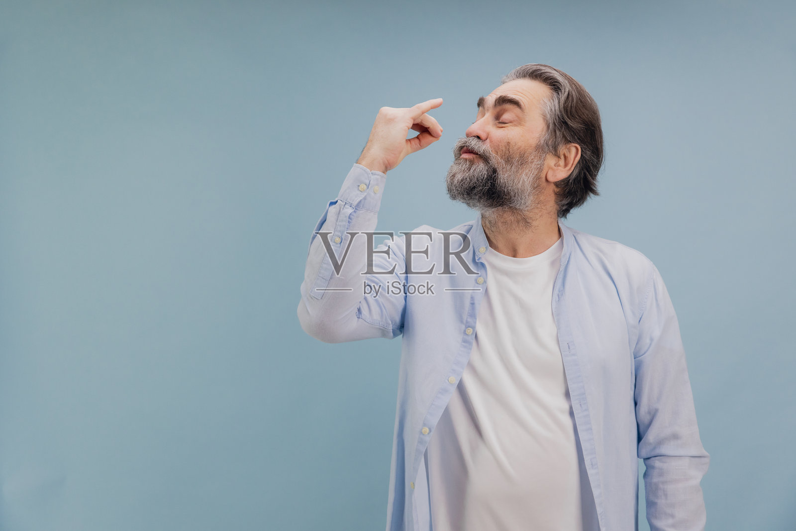 老年男子在蓝色背景下用手指夹着一个小物件照片摄影图片