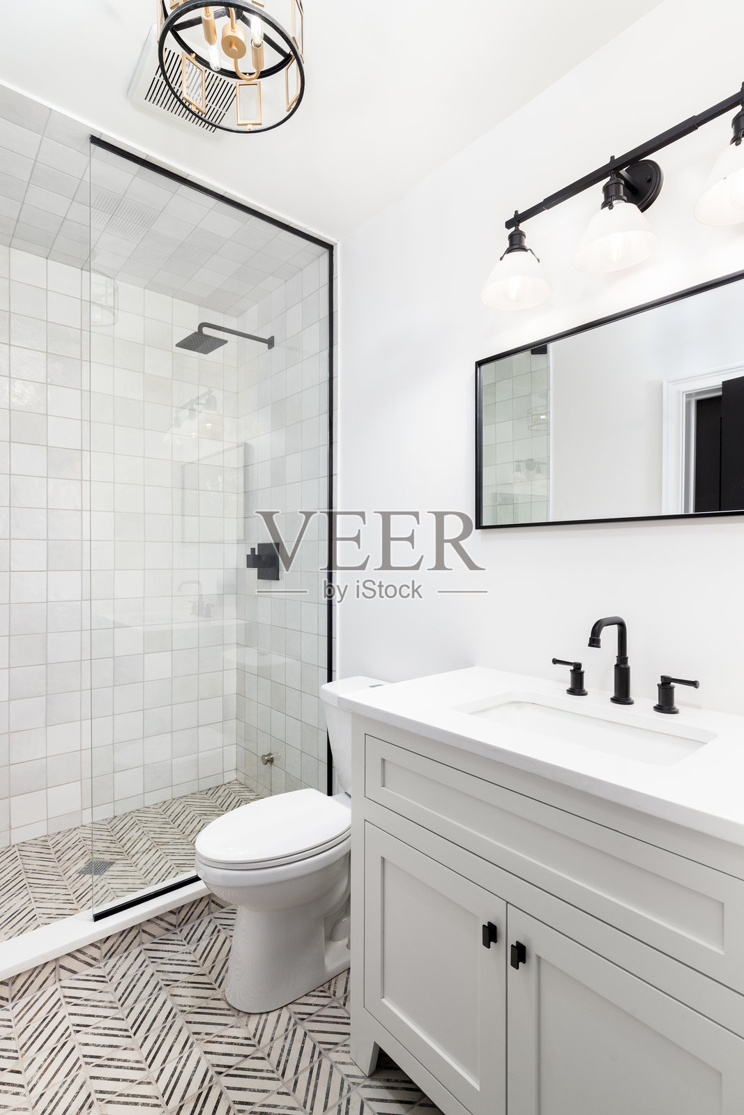 一间白色的浴室,配有黑色和金色的灯具,铺着瓷砖的地板和淋浴间。照片摄影图片