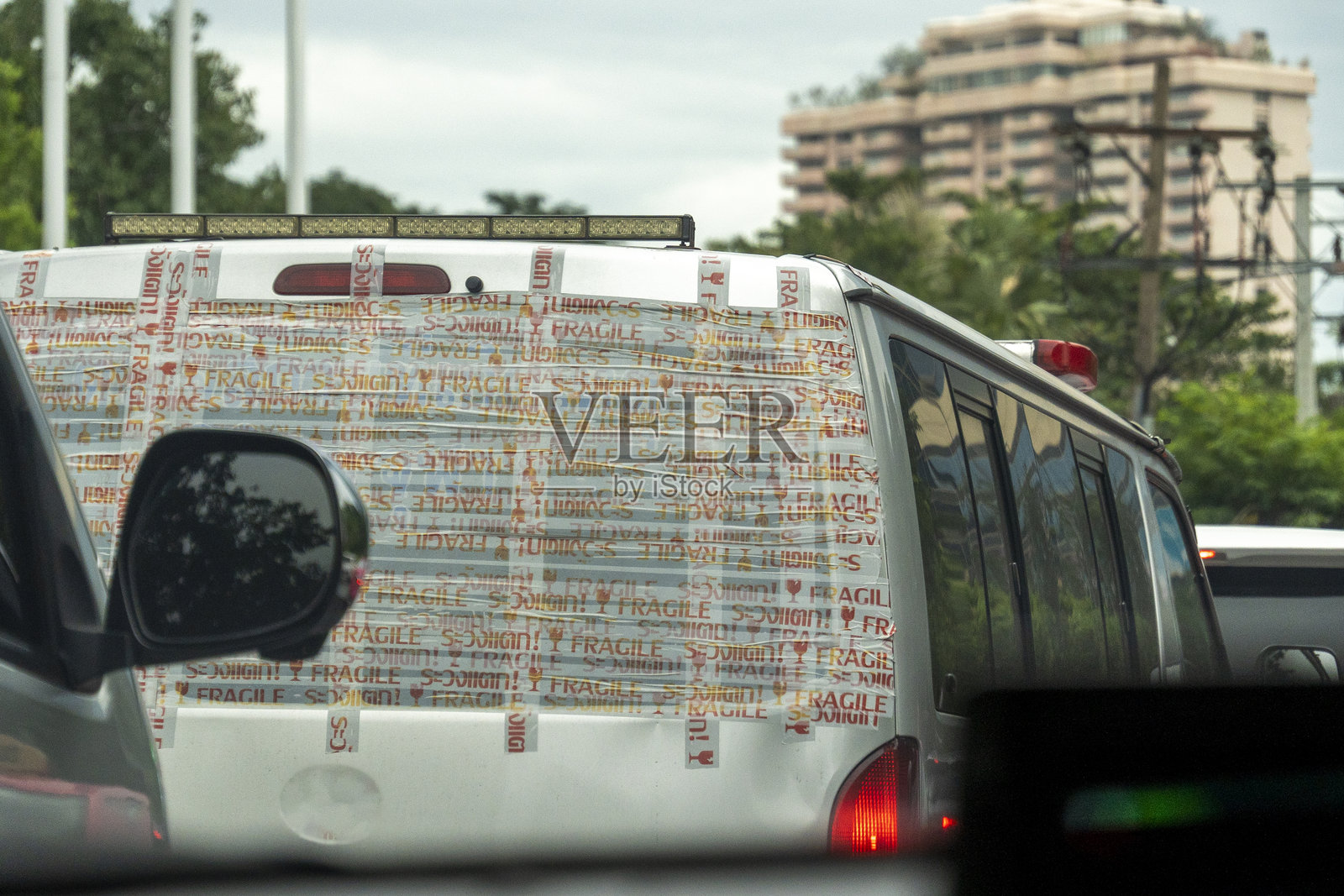 泰国曼谷 - 2024年12月22日:司机在城市繁忙街道上驾驶一辆贴满包装胶带和警告标签的面包车照片摄影图片