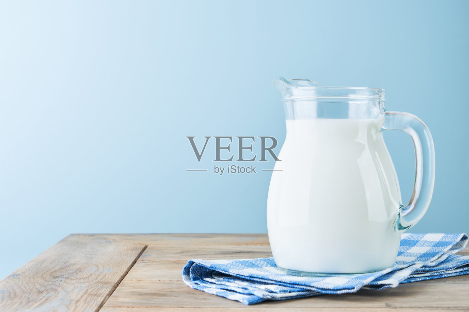 牛奶在木桌和蓝色背景的罐子和玻璃杯里。农场乳制品概念,奶日。厨房或超市的设计模型。副本的空间。照片摄影图片