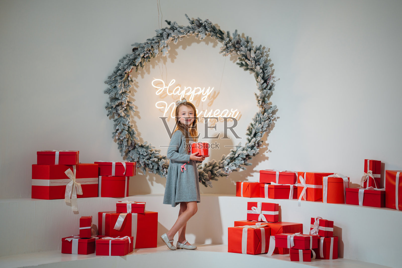 可爱的小女孩手捧红色礼物盒,周围是圣诞装饰。照片摄影图片