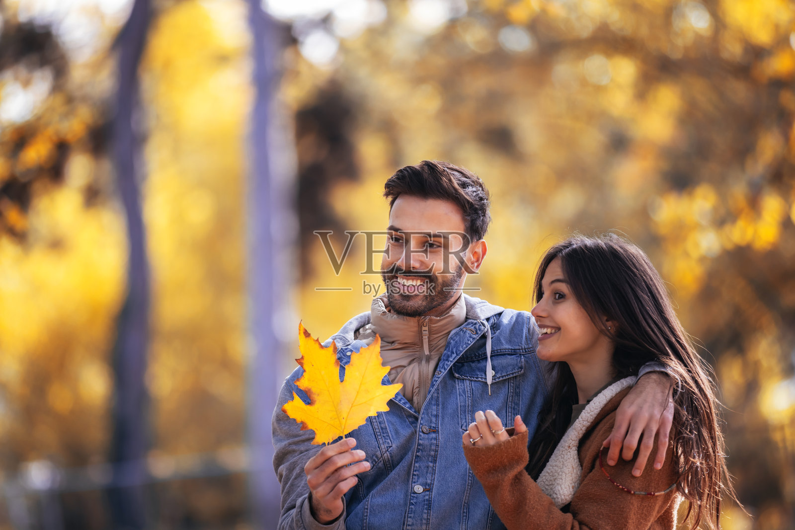 快乐的情侣在五彩斑斓的公园里散步。他们在秋天的日子里手里拿着橙色的树叶。照片摄影图片