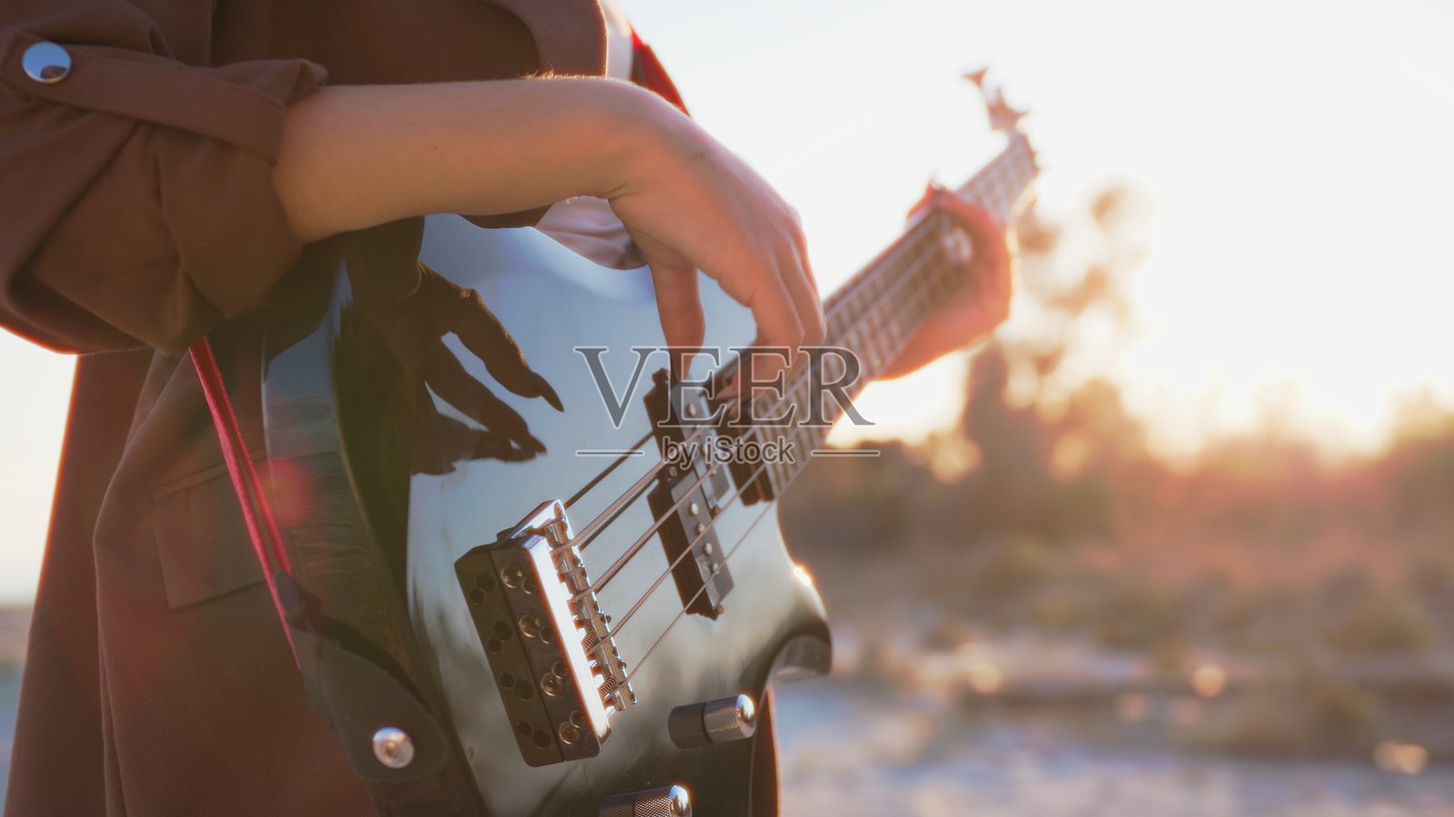 女孩在海滩日落时分靠近海洋演奏贝斯乐器照片摄影图片