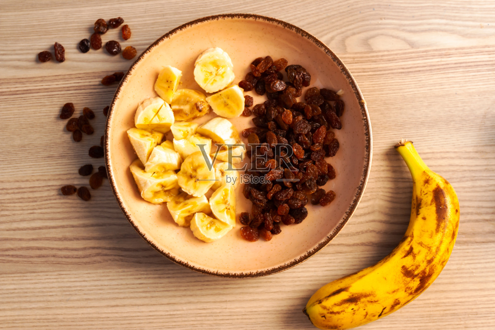 香蕉片和葡萄干放在木制背景的陶瓷盘子上。静物与有机健康食品。平的。前视图。关闭了。有选择性的重点。照片摄影图片