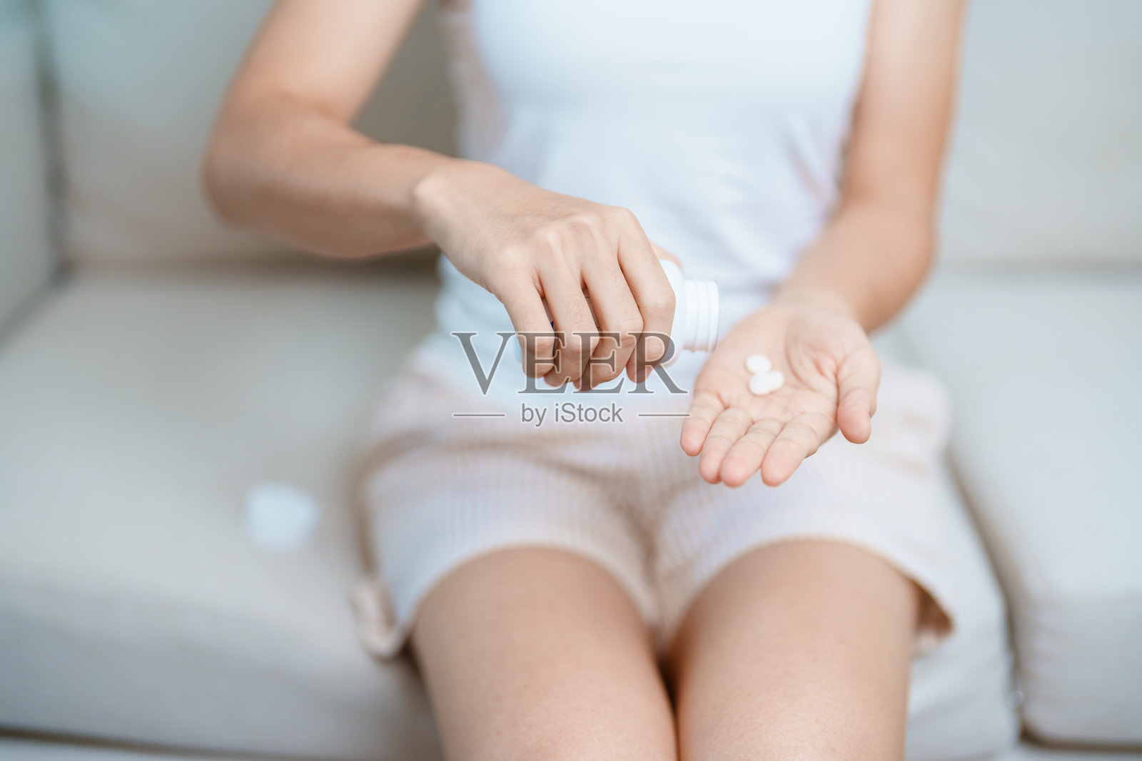 妇女在家里的沙发上手捧药止疼药,用于头痛、胃痛、腹泻、食物中毒、子宫内膜异位症、子宫切除术和月经照片摄影图片