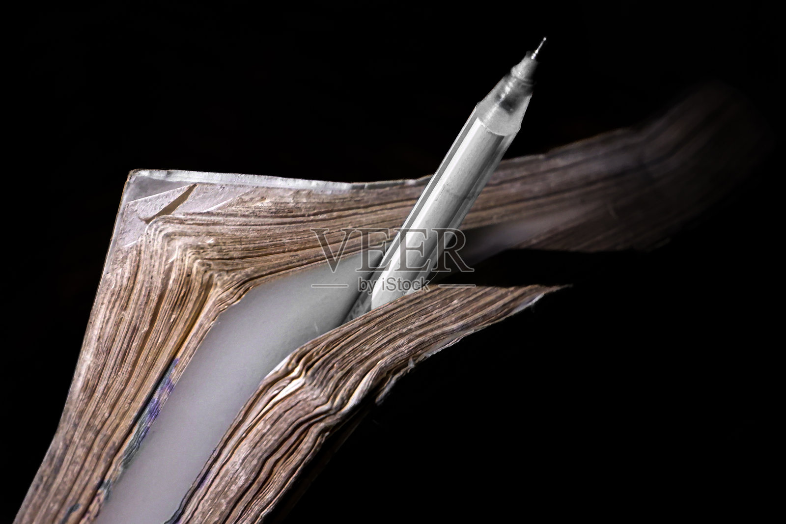 一支笔夹在一页书的中间,这支笔和厚厚的书也被岁月磨损了照片摄影图片