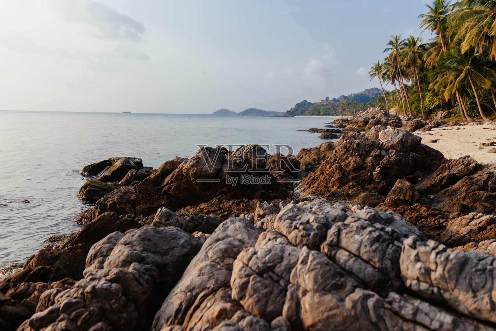 在日落时分,岩石海岸与小船和棕榈树构成了宁静的海滩照片摄影图片