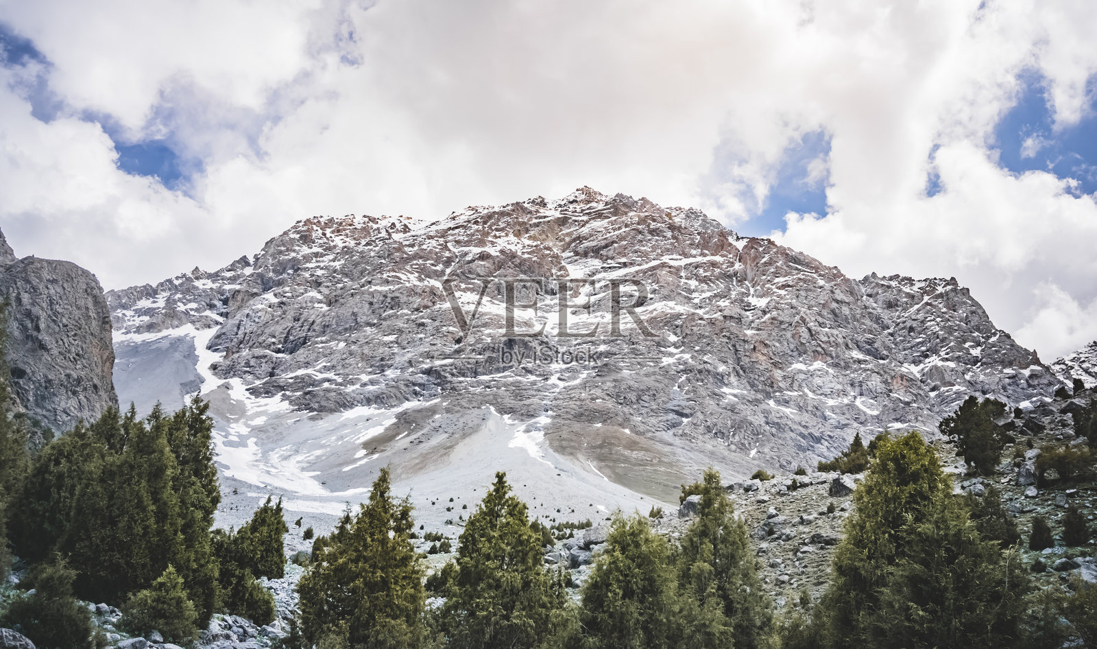 在一个阳光明媚的夏日,在塔吉克斯坦的范恩山脉,有岩石和碎石的山脉全景景观,有草地,雪和冰川照片摄影图片