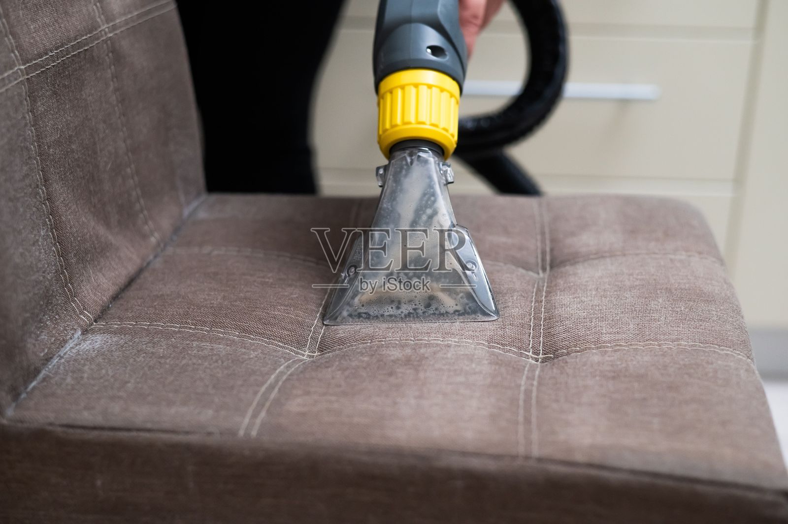 女性使用专业洗地吸尘器清洁布艺椅子。照片摄影图片