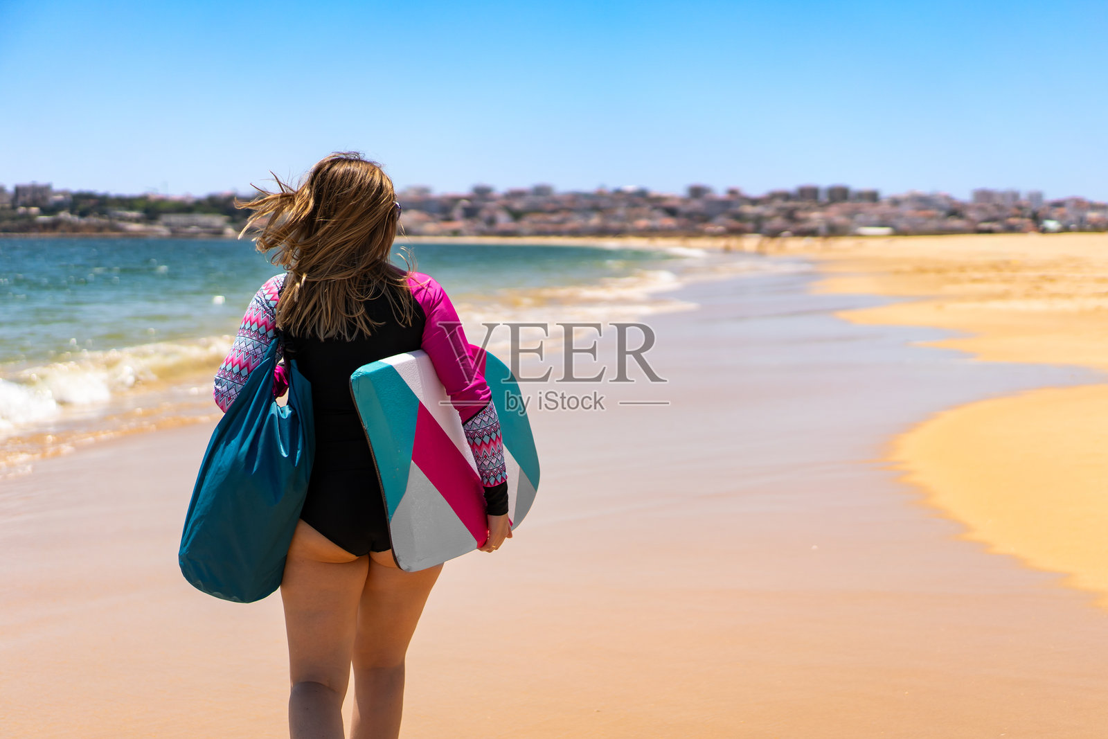 水上运动。穿着运动服的成熟的女性冲浪者手持冲浪板在沙滩上行走。照片摄影图片