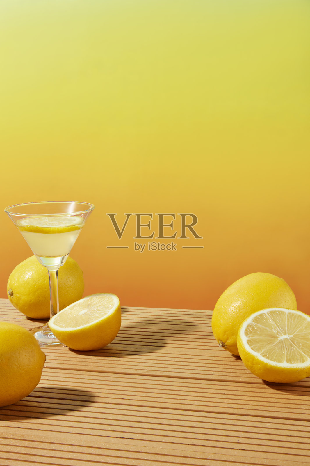 渐变的黄色背景与一些新鲜的柠檬和一个鸡尾酒杯柠檬汁特色的木制桌子。前视图照片与空白的空间表示照片摄影图片