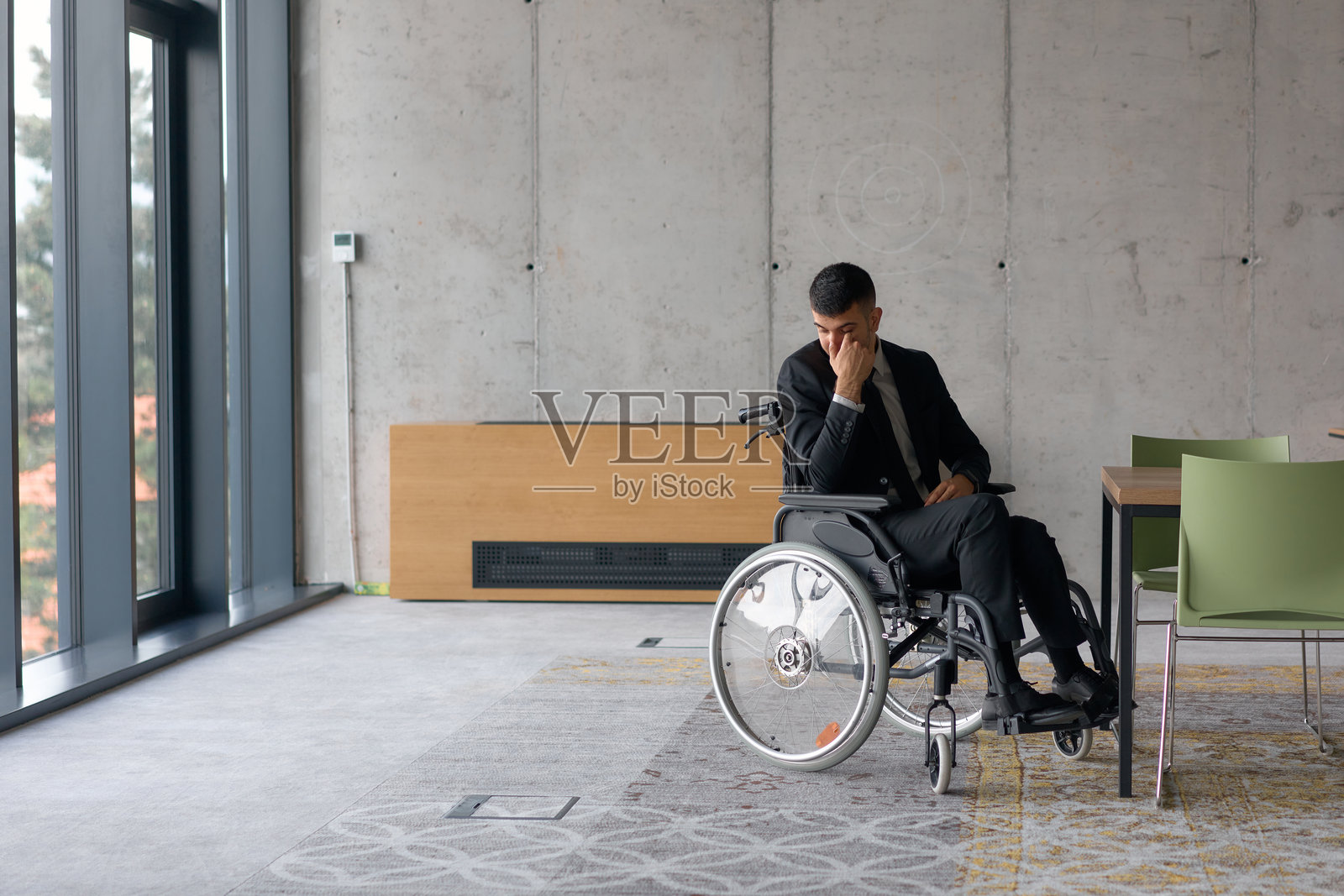 一位坐在轮椅上的悲伤失落的导演独自坐在宽敞的办公室里,思考着与职业责任相关的挑战和孤独感。照片摄影图片