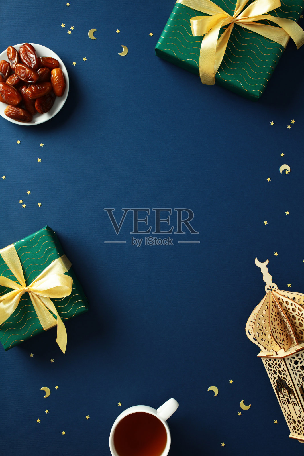 拉马丹快乐,穆斯林节日竖幅设计,背景为深蓝色,包含日期、礼品盒、阿拉伯灯笼、茶杯和五彩纸屑。平铺,俯视,留白空间。照片摄影图片