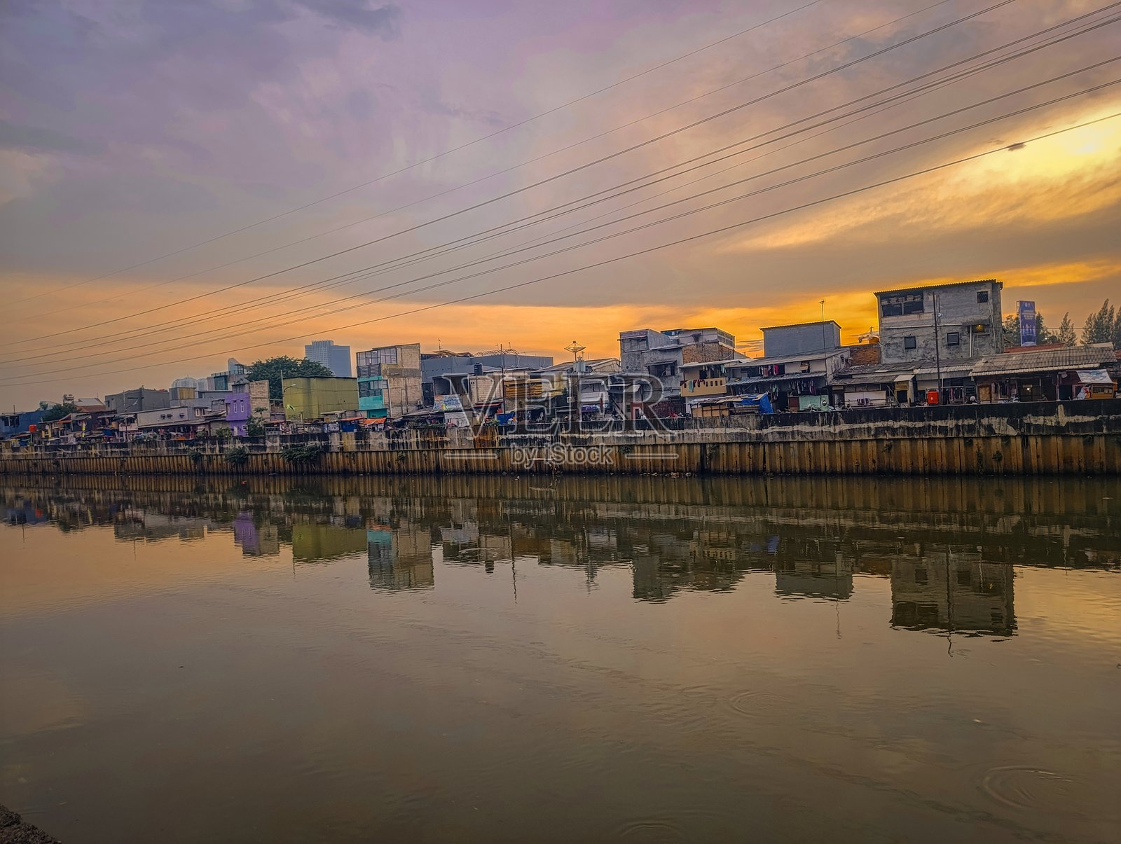 雅加达日落时分的多彩河岸景观,绚丽的天空色彩映照在水面上。传统与现代建筑的结合展示了这座城市的建筑多样性。照片摄影图片