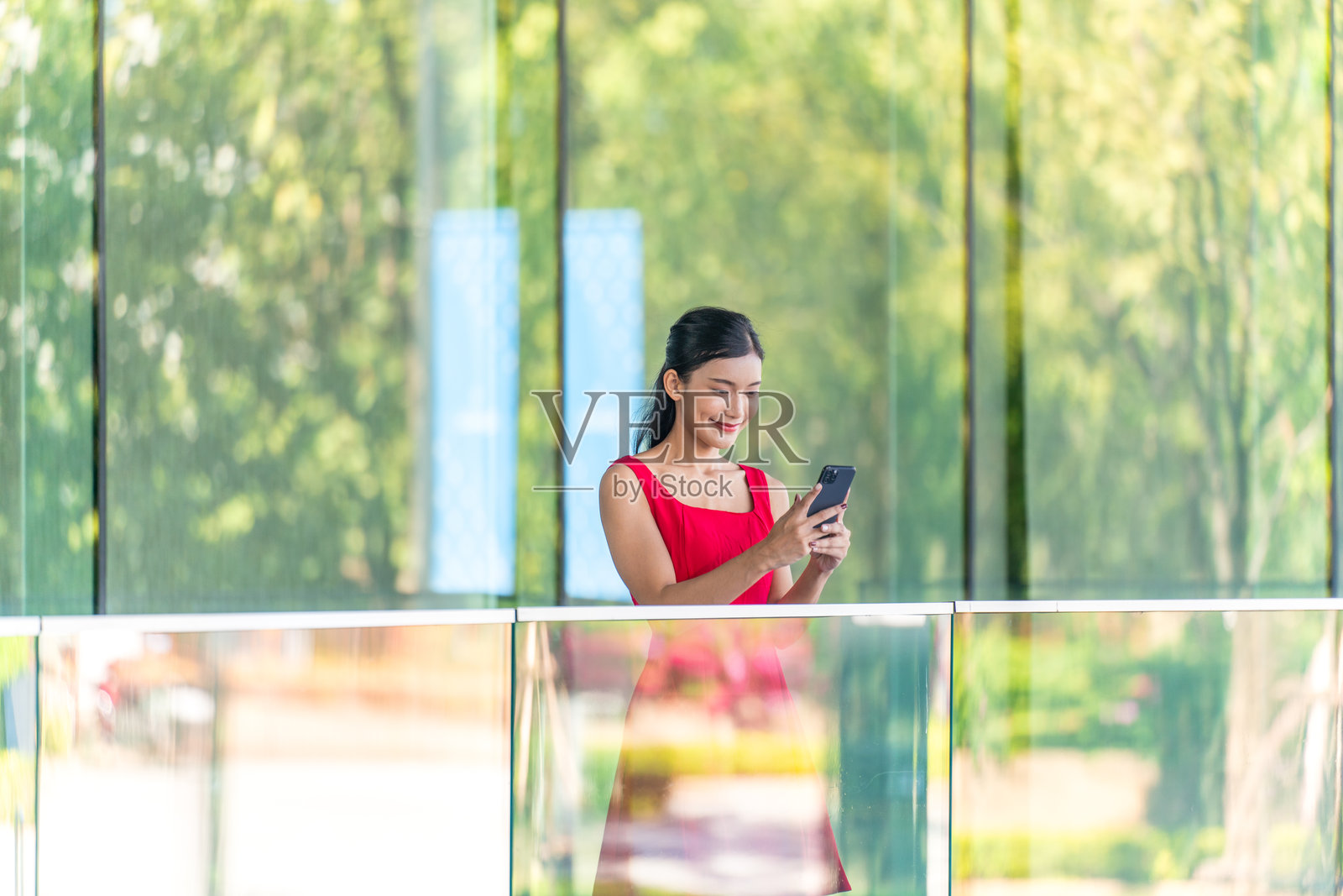 身穿红色连衣裙的年轻女商人在现代玻璃办公楼前户外使用手机照片摄影图片
