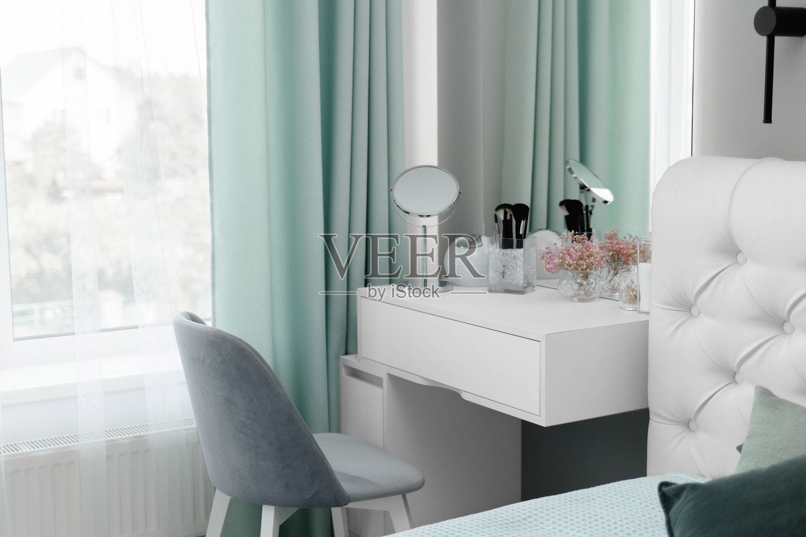 化妆刷放在梳妆台上的一个立式花瓶里。梳妆台的设计位于一个优雅的现代卧室中。卧室的化妆角落。室内极简设计。照片摄影图片