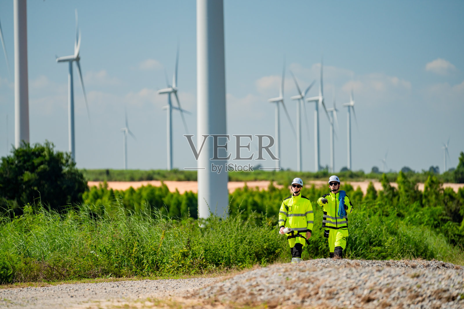 工人在阳光明媚的乡村地区检查可再生能源场地,风力涡轮机矗立其中。照片摄影图片