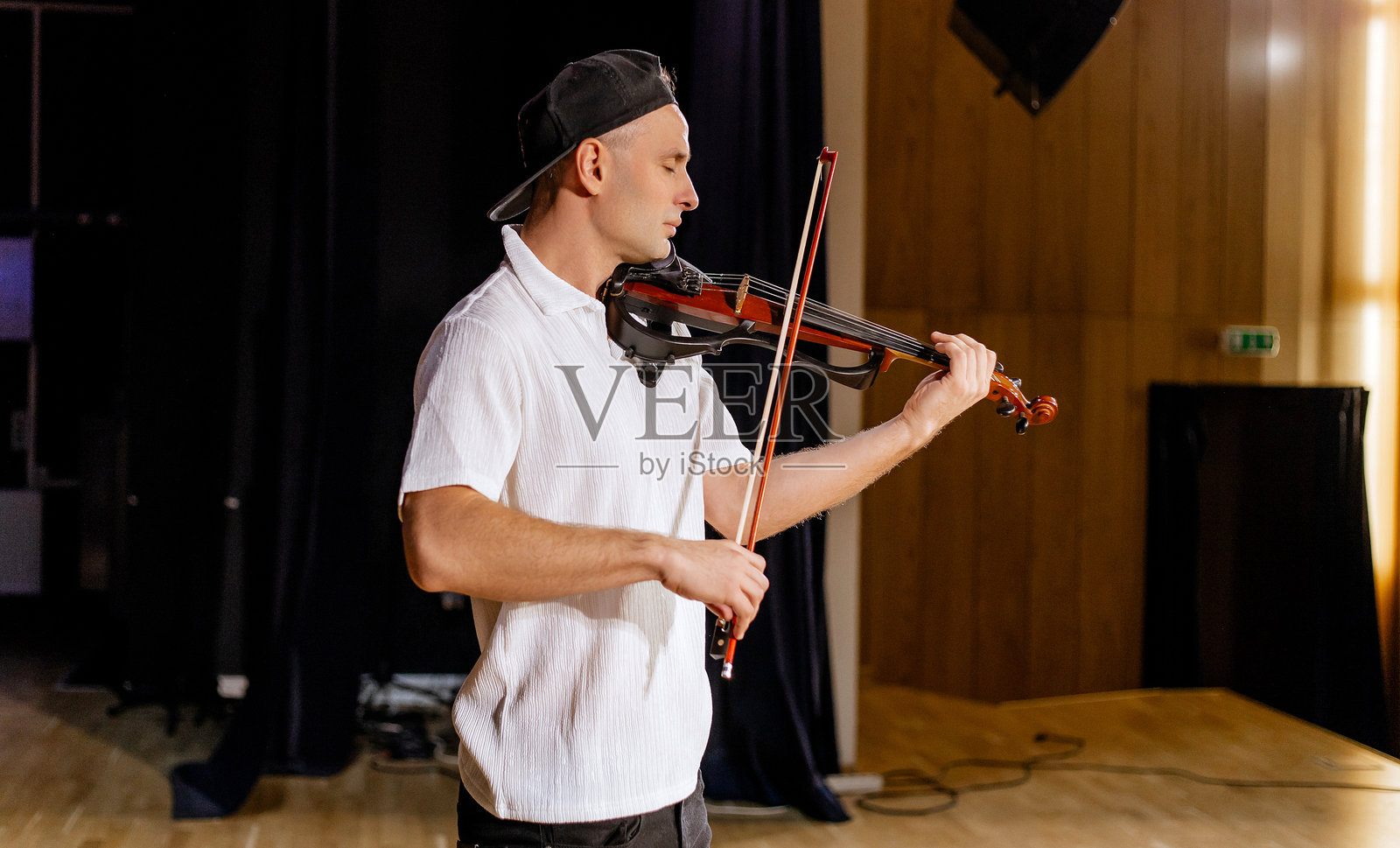 一位40岁的男子穿着白衬衫和黑色帽子,站在黑色背景前,愉快地拉着小提琴,场景中有音乐元素。男性小提琴手,留有空白空间。照片摄影图片