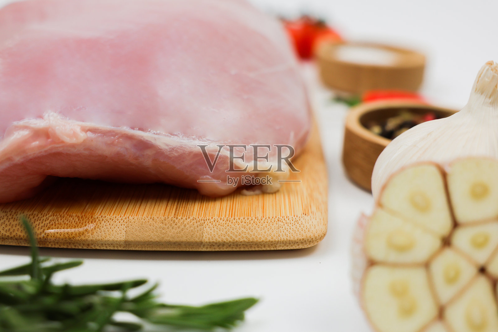 一块火鸡胸肉的特写侧视图,放在白色背景上的木砧板上,周围环绕着调料、香草和蔬菜。健康饮食、膳食和天然产品、烹饪的概念。照片摄影图片
