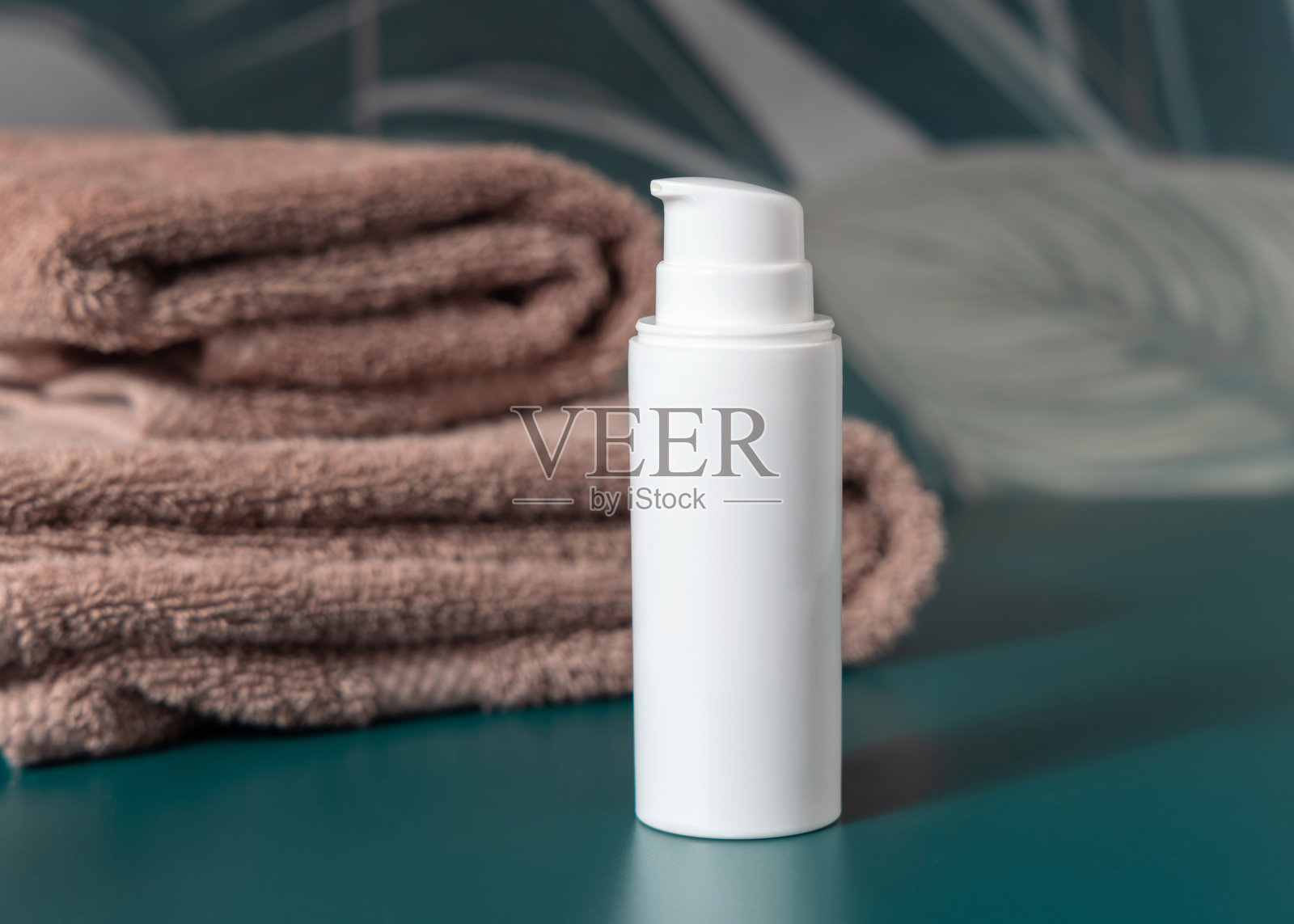 深绿色热带浴室中,白色乳霜瓶靠近棕色毛巾的特写,化妆品样机照片摄影图片