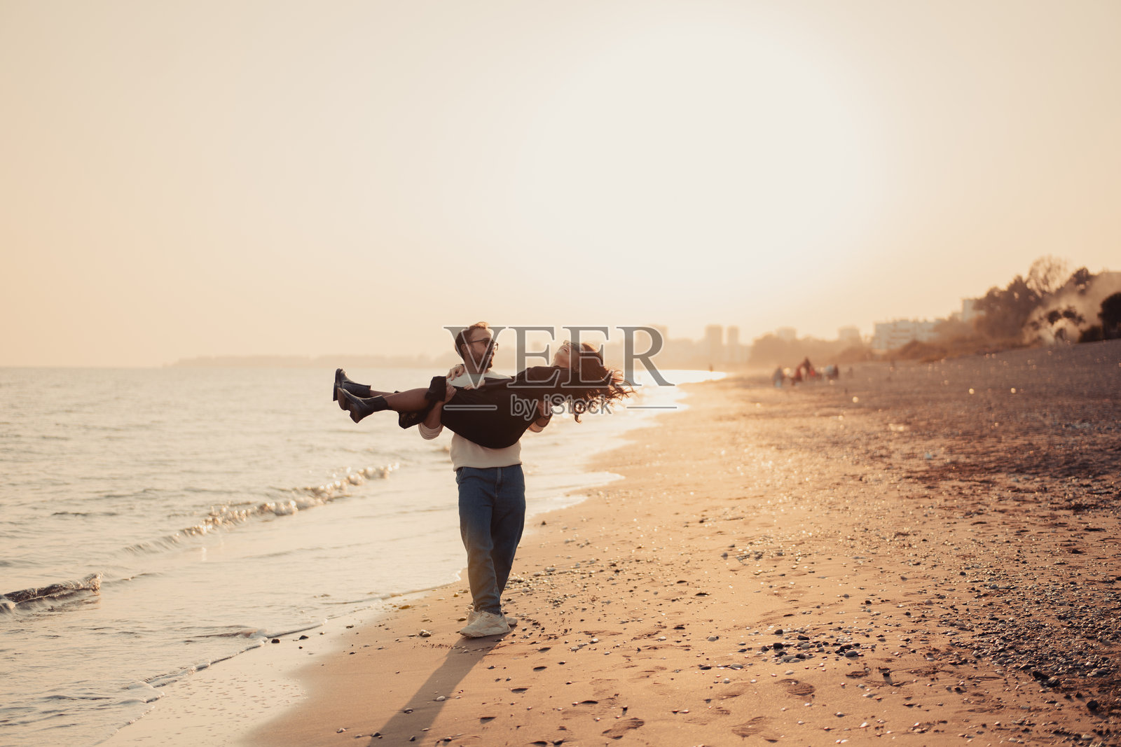 年轻男子在日落时分抱着女子走在海滩上照片摄影图片