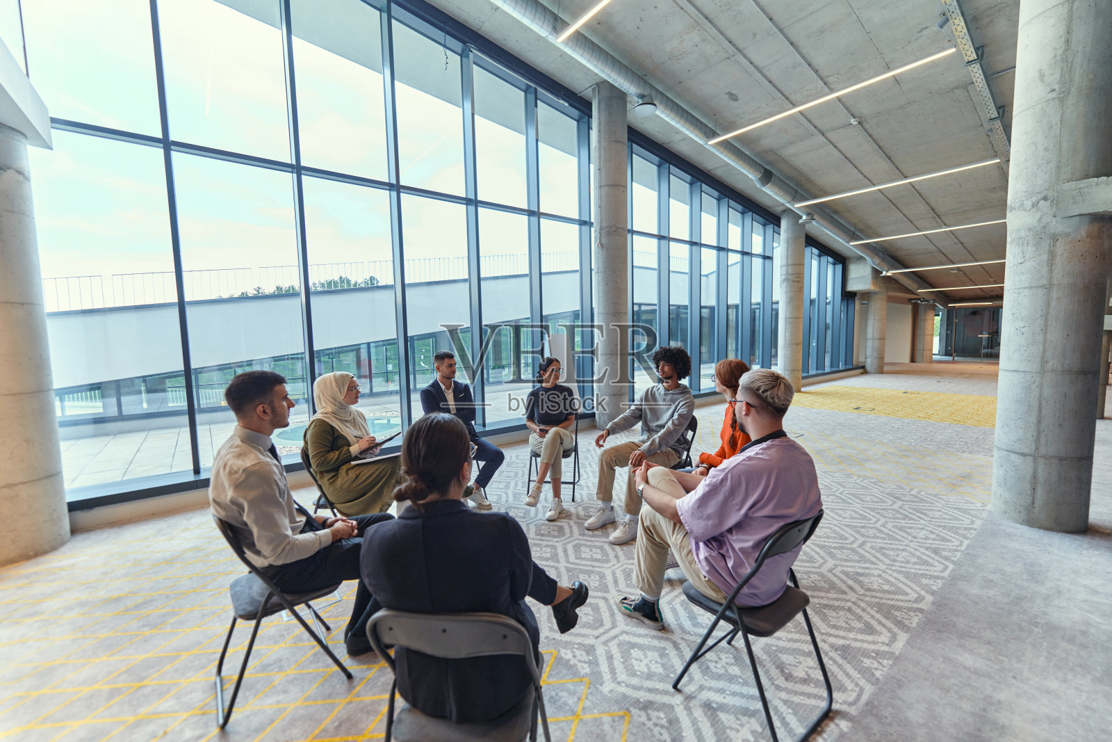 一群多元化的年轻企业家围成一圈开会,讨论大型企业中的公司挑战和创新解决方案。照片摄影图片