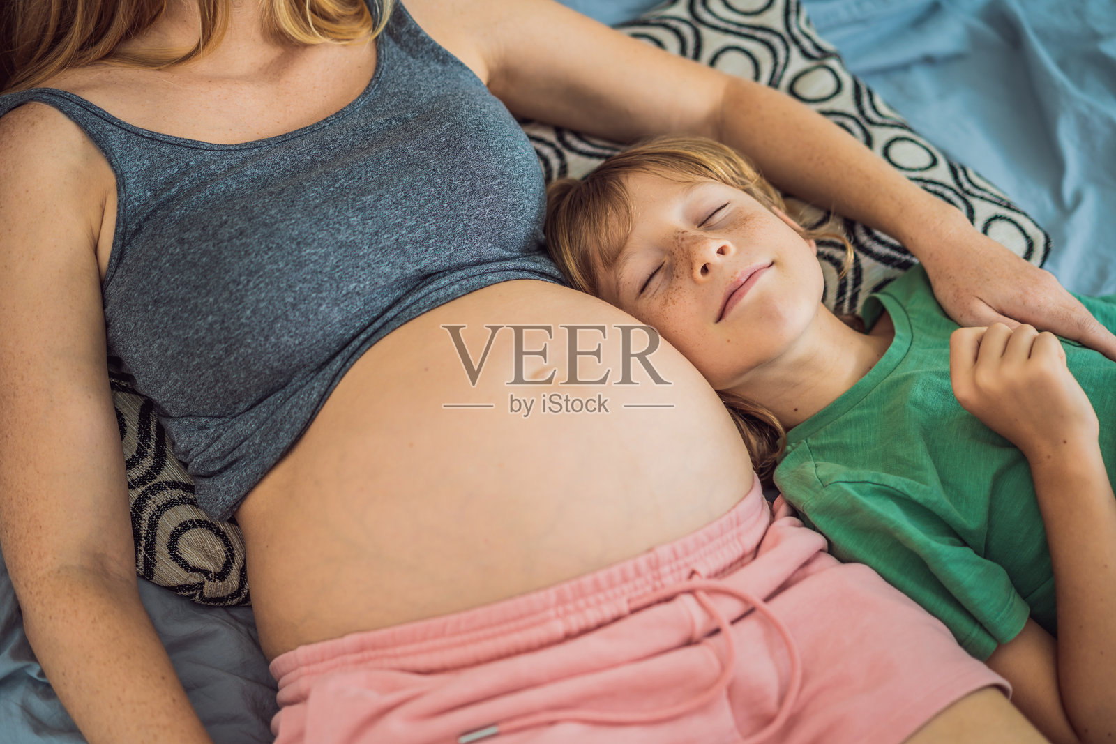 年轻漂亮的孕妇和她的大儿子。可爱的男孩把耳朵贴在妈妈的肚子上。期待家庭中新成员的概念。为大孩子准备迎接小宝宝。照片摄影图片