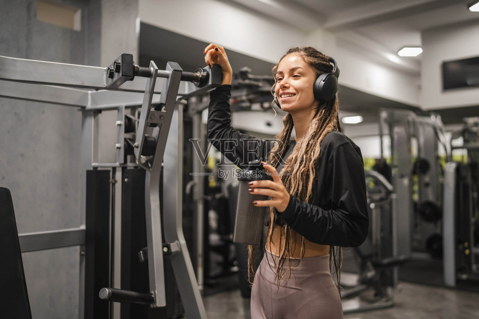 年轻女性戴着耳机,手持摇摇杯,正在休息锻炼。照片摄影图片