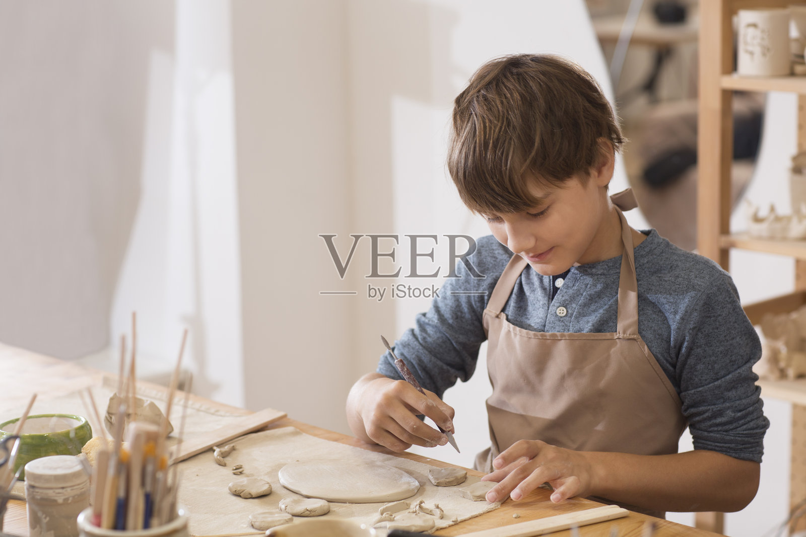青少年男孩在陶艺学校用粘土制作陶瓷盘子。儿童在工作坊参加艺术与手工艺课程。照片摄影图片