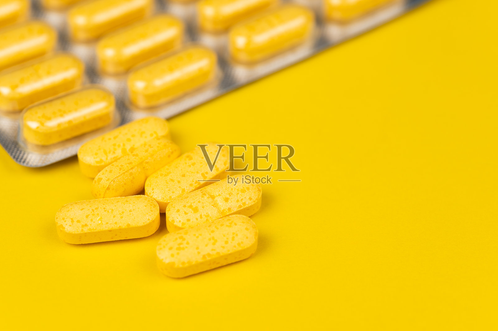 黄色背景上散落着的黄色药片和一个药板包装照片摄影图片