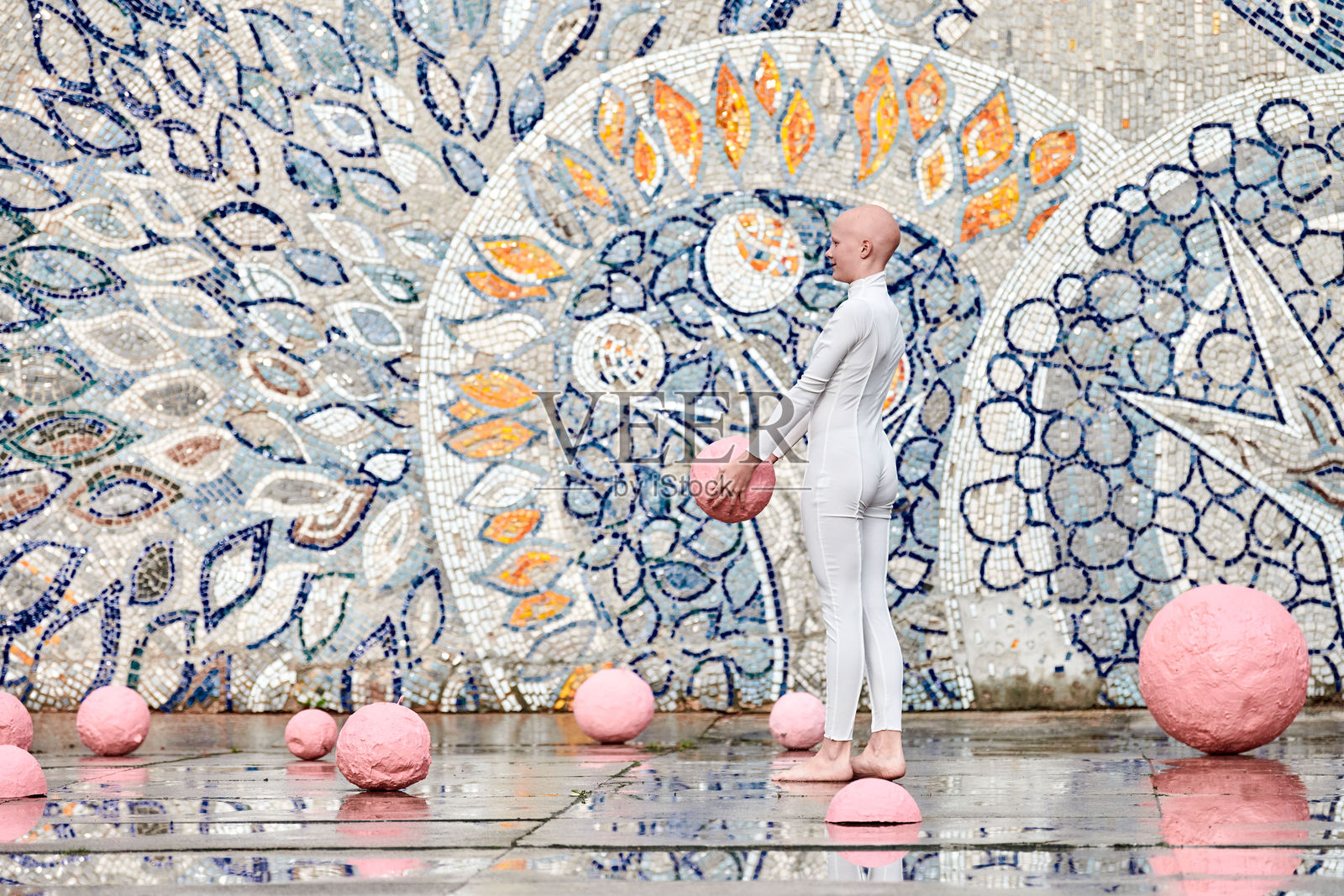 年轻的无毛女孩穿着白色未来主义套装,在户外跳舞,手里拿着粉色球。照片摄影图片