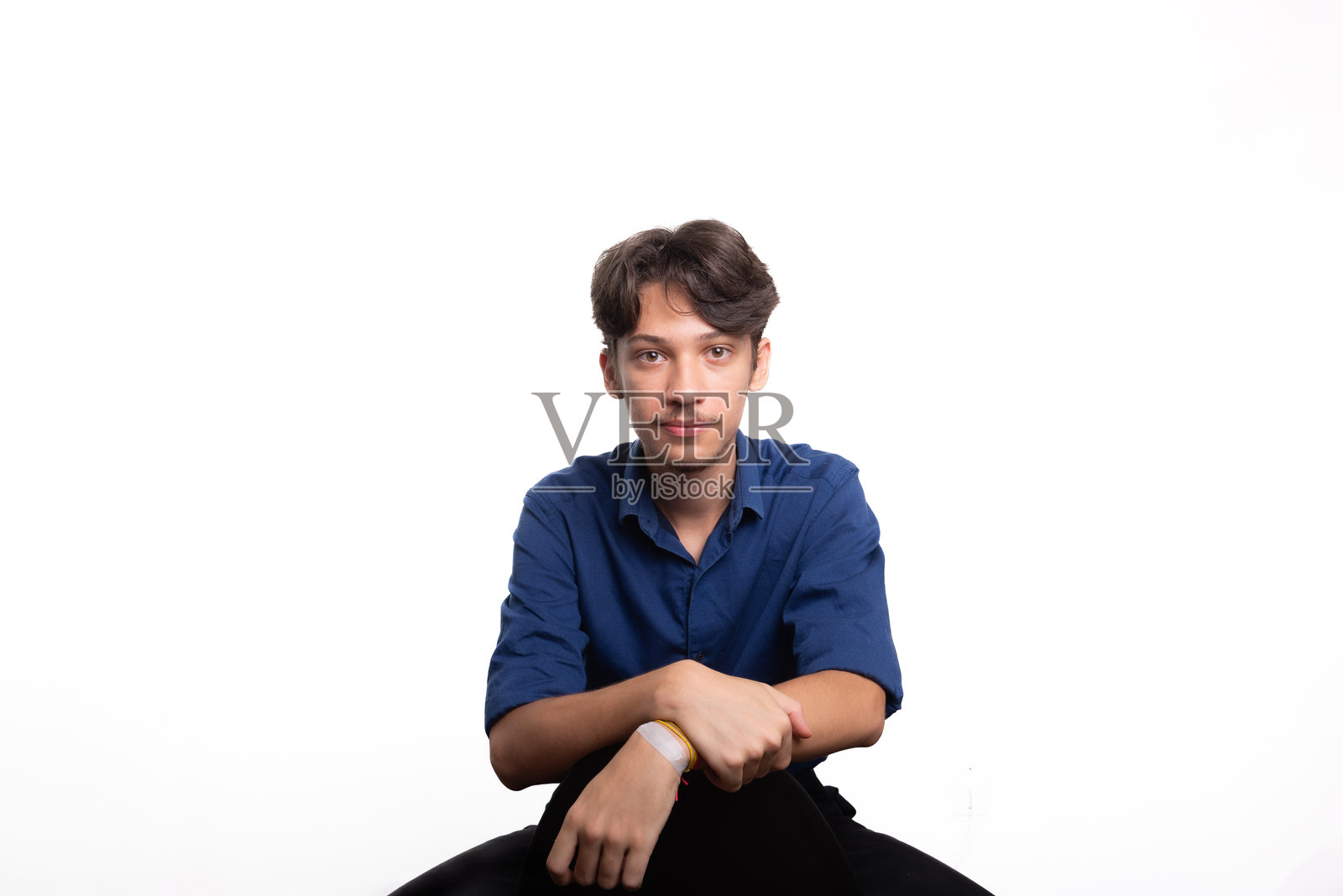 年轻帅气的学生,黑发蓝衬衫,坐着,认真地看着镜头。背景为白色。自信的人。照片摄影图片