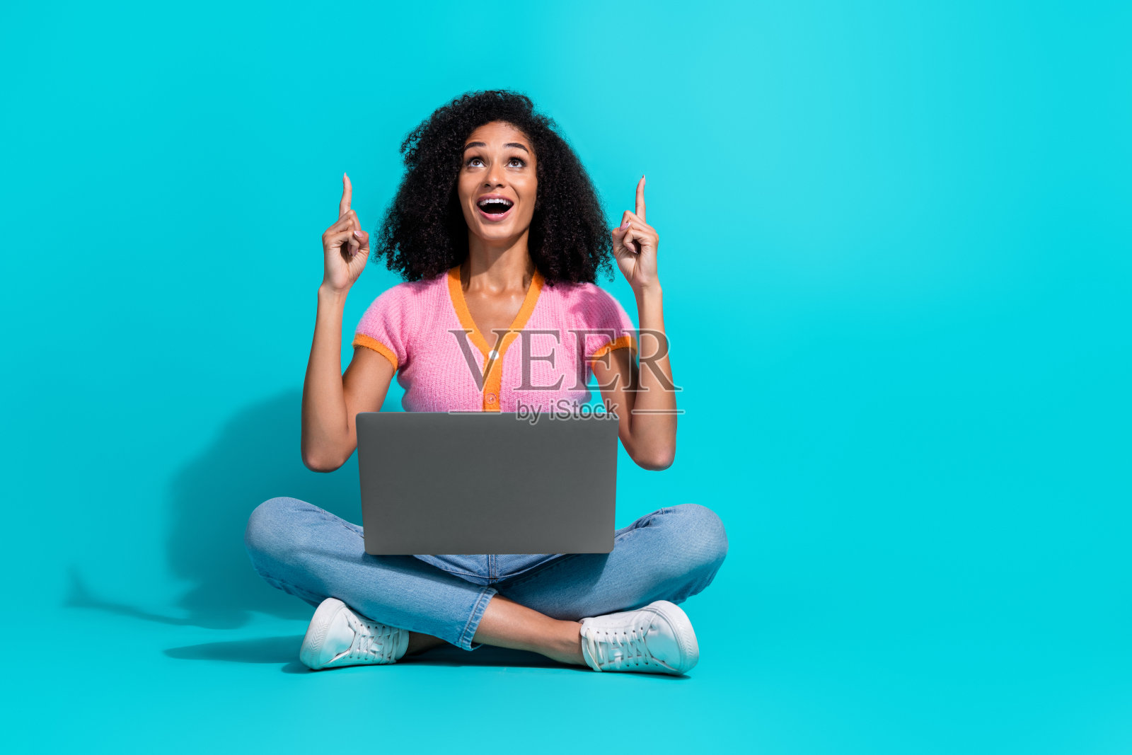 愉快的年轻女性盘腿坐在湖蓝色背景前,手势表达兴奋和快乐照片摄影图片