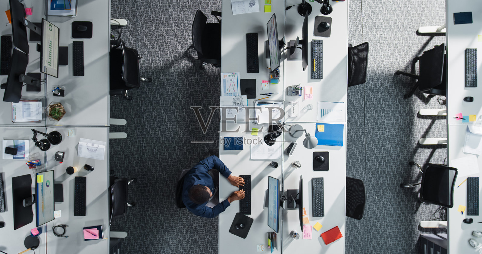 从上方俯视一位非裔美国男性员工在公司办公室加班。他正在使用台式电脑分析财务数据,为高级管理层创建报告。照片摄影图片