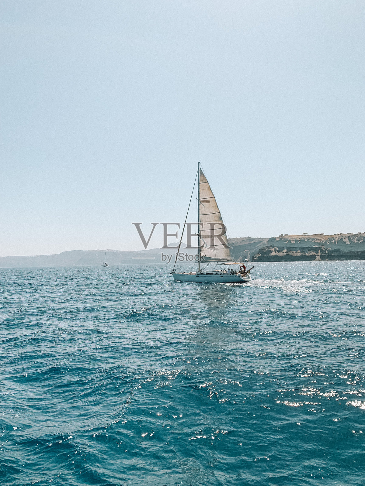 宁静的照片,展示了一艘船在希腊圣托里尼附近的爱琴海上滑行,背景中可见岛屿标志性的悬崖。照片摄影图片