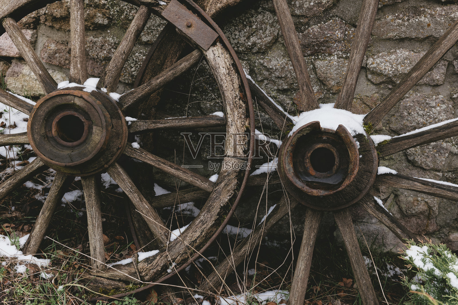 冬季雪地中,旧木制马车轮靠在石墙上。照片摄影图片