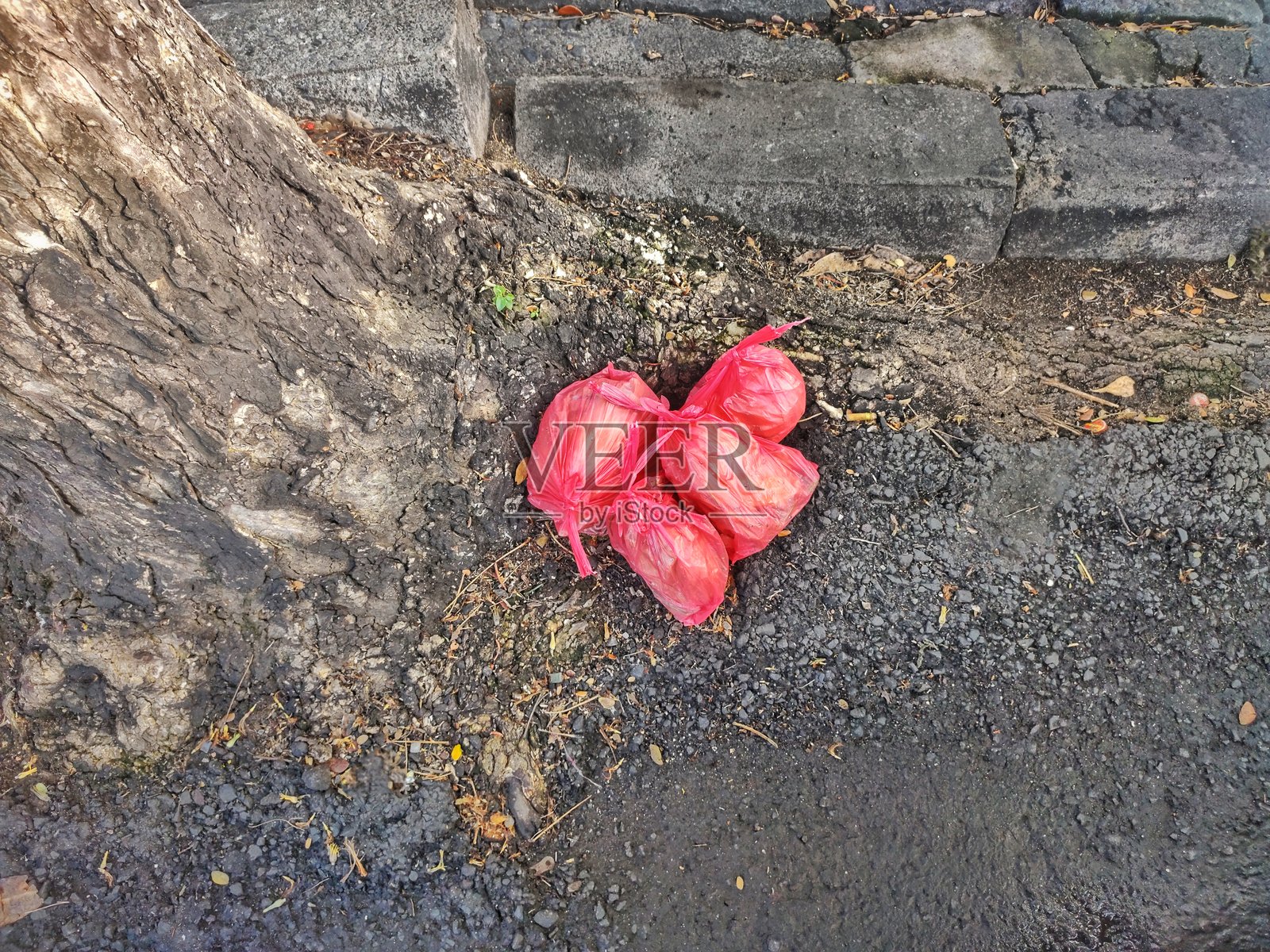 红色塑料垃圾袋被丢弃在树旁的街道上照片摄影图片