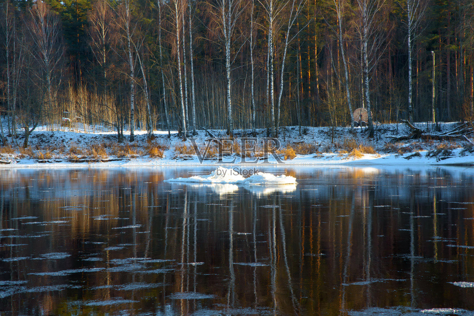 冬季河流场景,漂浮的冰块,平静的水面映照着光秃的树木,背景是覆盖着雪的河岸。照片摄影图片