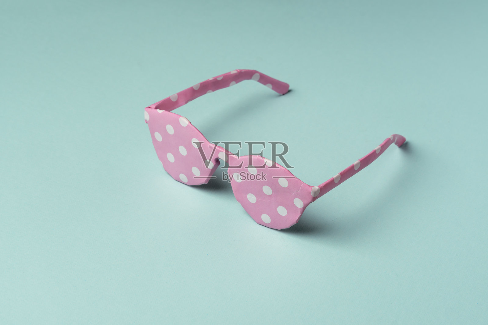 粉色波点纸包裹的太阳镜放在蓝色背景上。创意礼物、惊喜、夏季时尚和独特包装的概念。照片摄影图片