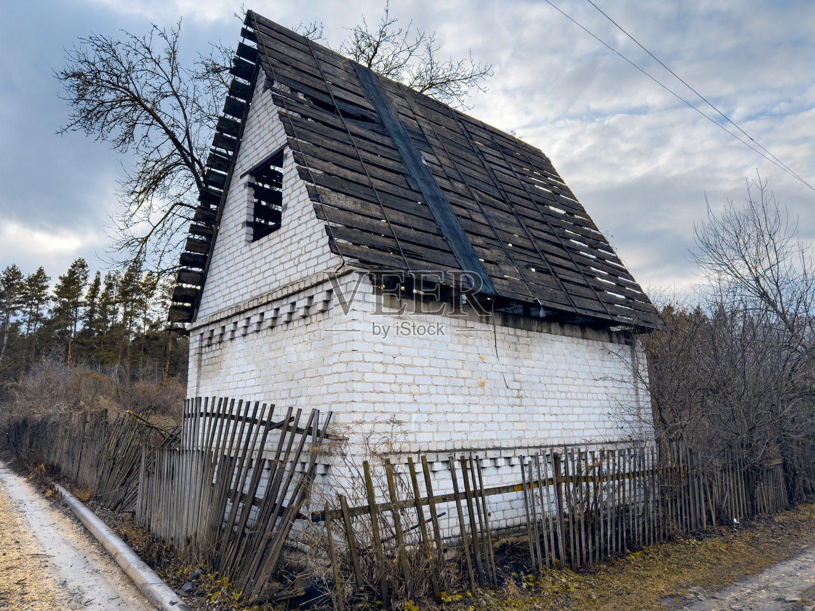一座小而古老的白色房子,带有倾斜的屋顶和木栅栏照片摄影图片