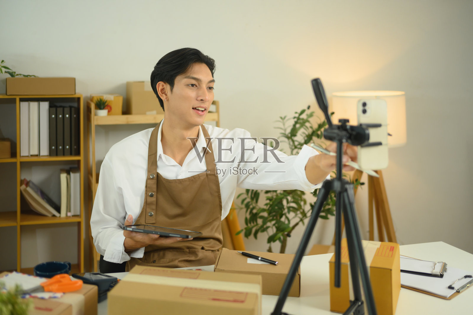 年轻的企业主正在调整三脚架上的智能手机,以便进行在线直播产品销售。照片摄影图片