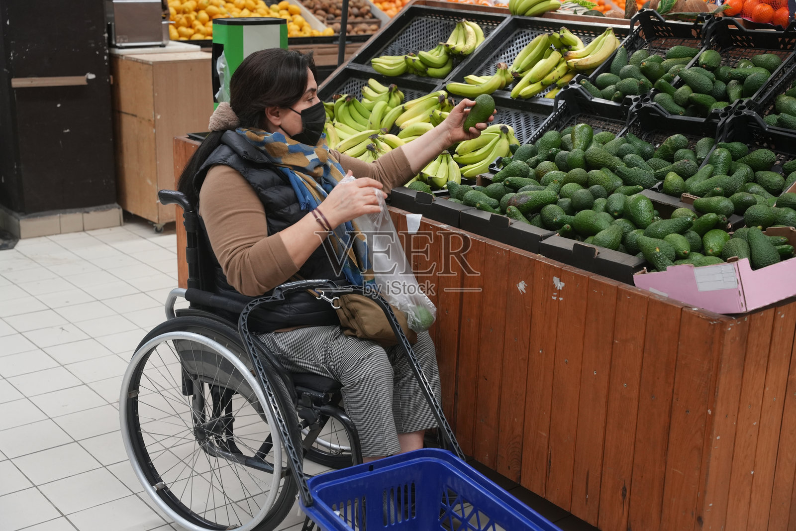 一位坐在轮椅上的女性在杂货店挑选鳄梨。照片摄影图片