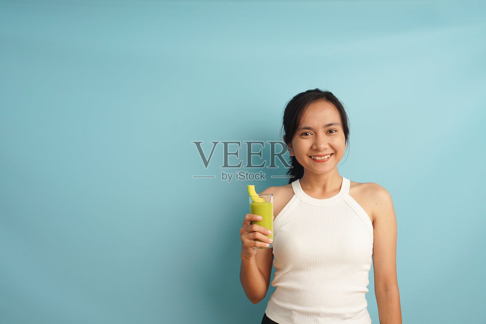 女人手持蓝色背景下的牛油果冰沙杯照片摄影图片
