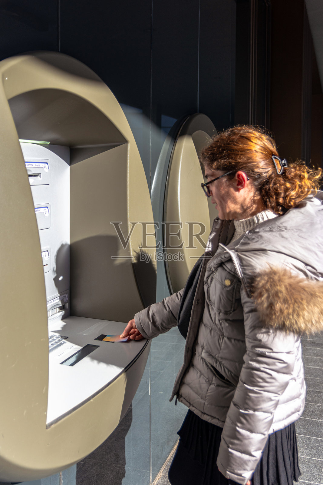 穿着冬季服装的女性在阳光明媚的日子里使用户外自动取款机照片摄影图片