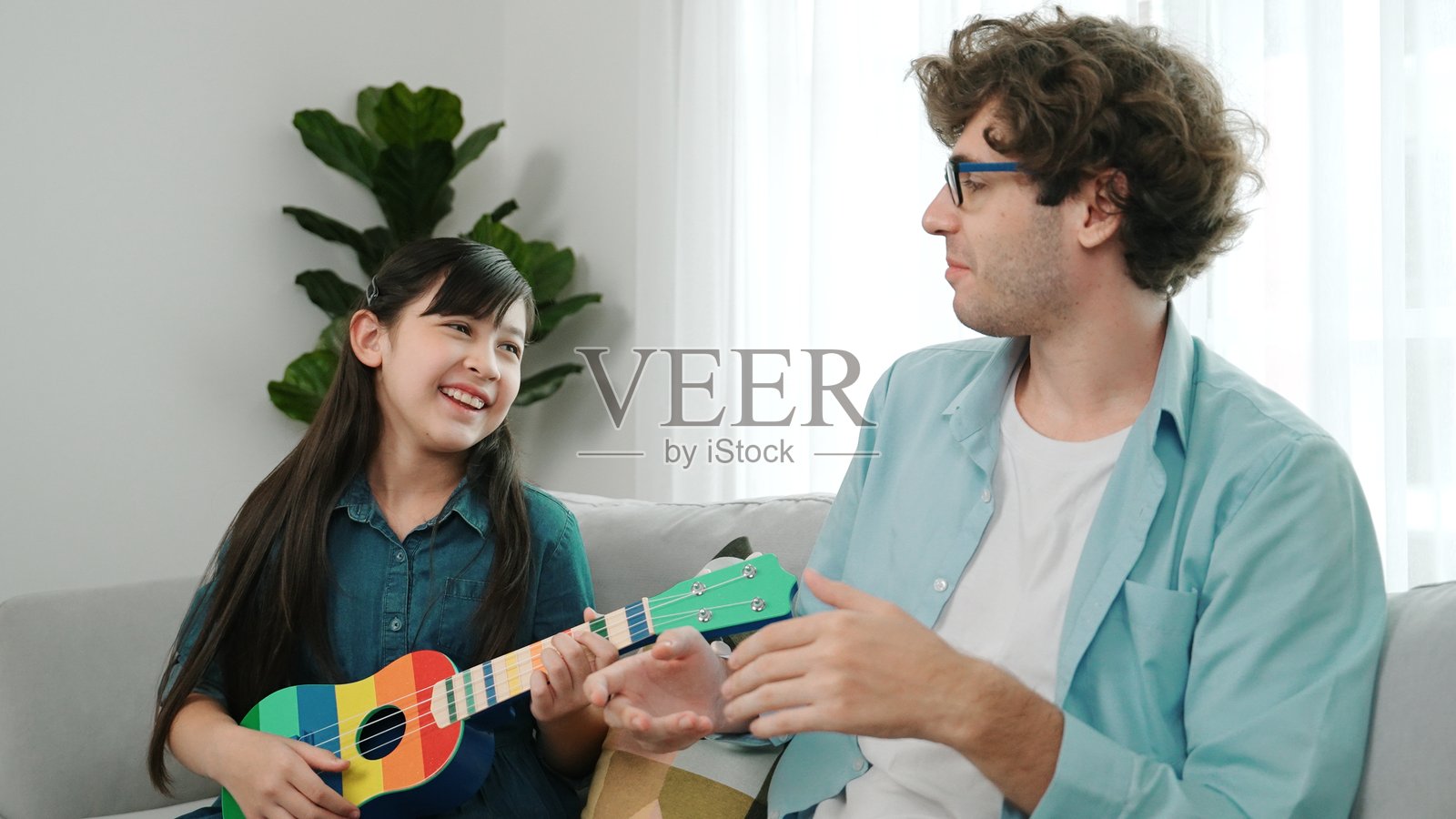 父亲温暖地看着聪明的女儿在弹尤克里里。教育学。照片摄影图片