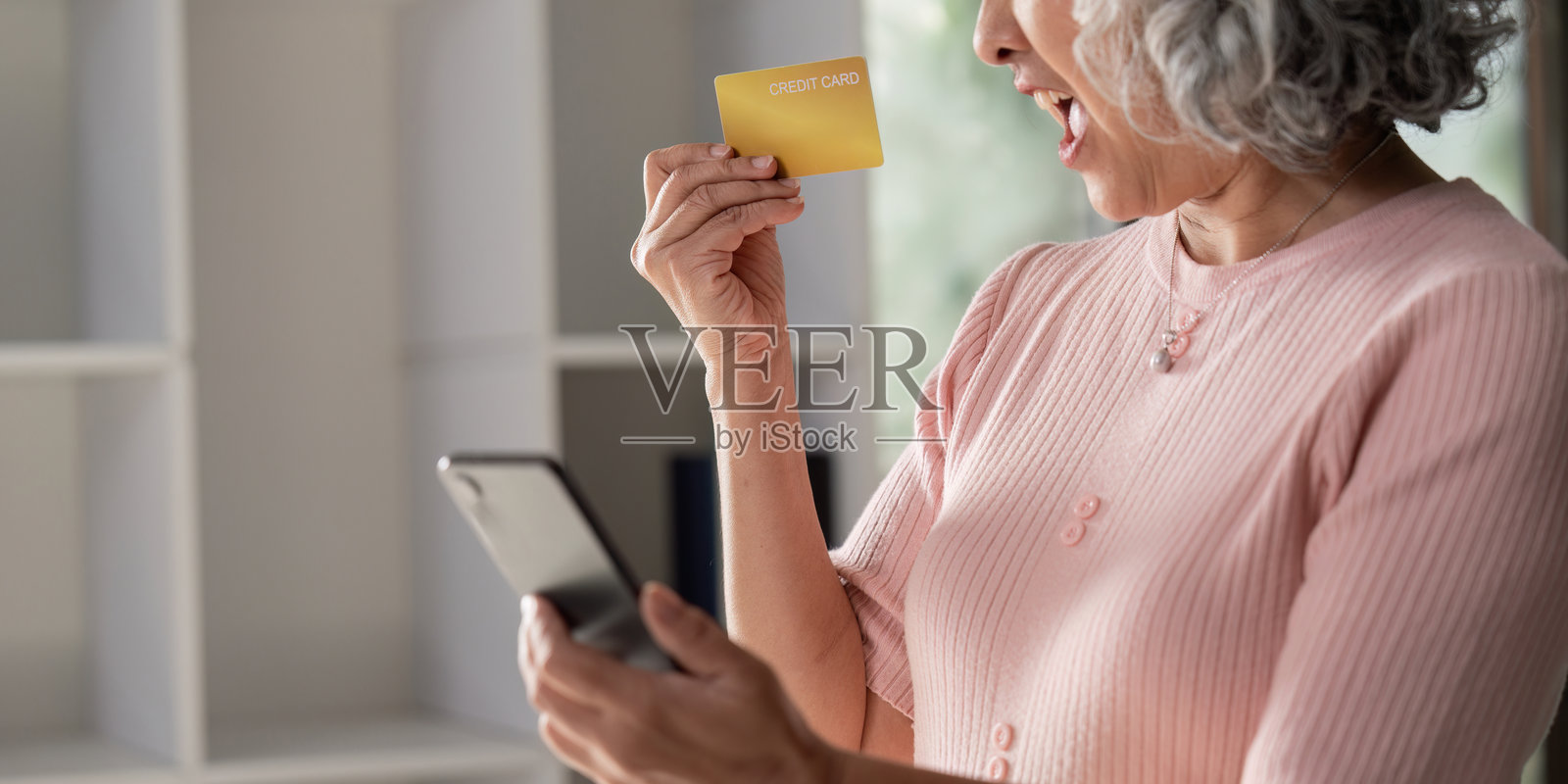 兴奋的老年女性在网上购物,手里拿着信用卡和智能手机。照片摄影图片
